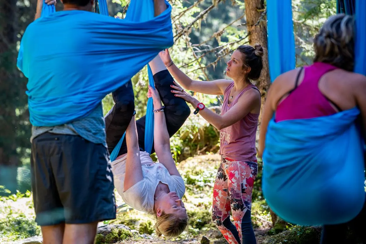 Gaëlle installe une participante dans un hamac de yoga aérien, en plein air sous les arbres