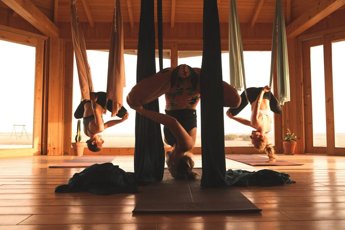 Trois élèves la tête en bas dans leurs hamacs, pendant un cours de yoga aérien